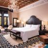 El Hotel Alfonso XIII Sevilla cuenta con un elegante dormitorio con lámpara de araña, cama de gran tamaño y suelo estampado, complementado con muebles clásicos y tonos neutros. - ForTwo - Planes para parejas