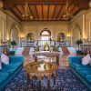 El opulento interior con una decoración ornamentada, sofás azules y una mesa redonda central se asemeja al elegante Hotel Alhambra Palace Granada, con entradas arqueadas que reflejan la grandeza de Granada. - ForTwo - Planes para parejas