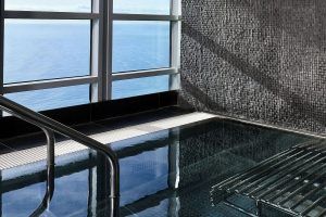 El Desayuno, Spa de Lujo y Masaje: La Experiencia Total en el Hotel Arts (Barcelona) cuenta con una piscina cubierta con mosaicos y barandillas metálicas, que ofrece impresionantes vistas al mar a través de grandes ventanales. - ForTwo - Planes para parejas