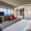Disfrute de la comodidad del Hotel Barceló Málaga con una lujosa cama king, un cómodo sillón rojo y un elegante televisor de pantalla plana. El elegante baño con paredes de cristal esmerilado realzará su estancia en la vibrante Málaga. - ForTwo - Planes para parejas