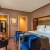 Elegante habitación en el Hotel Casa Fuster GL Monumento en Barcelona con una cama grande, lujosas sillas azules, escritorio de madera, iluminación cálida; las puertas evocan el encanto de la arquitectura del Monumento. - ForTwo - Planes para parejas