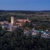 Vista aérea del Hotel Castell d'Emporda (Girona) iluminado y estructuras cercanas enmarcadas en el paisaje rural al anochecer. - ForTwo - Planes para parejas