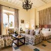Una elegante habitación en el Hotel Castillo de Santa Catalina Málaga cuenta con una cama doble, muebles con motivos florales, una lámpara de araña y ventanas altas con cortinas largas. - ForTwo - Planes para parejas