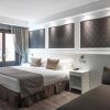 Descubra el encanto de Barcelona en las modernas habitaciones del Hotel Catalonia Magdalenes, que cuentan con una cama grande, paneles de pared decorativos, un acogedor sofá, ventanas con cortinas y elegantes mesitas de noche. - ForTwo - Planes para parejas