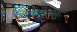 El elegante dormitorio imita una suite del Hotel Indiana (Madrid), con una lujosa cama, un sofá azul, arte mural vibrante, tragaluz y un televisor que muestra una escena de película, ofreciendo el ambiente elegante que esperarías en Madrid. - ForTwo - Planes para parejas
