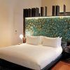 Descubra la elegancia de una habitación moderna en el Hotel Mercer (Sevilla), que incluye una cama grande con un cabecero ornamentado, un pequeño escritorio con espejo y una iluminación cálida para una relajación y comodidad máximas. - ForTwo - Planes para parejas