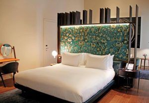 Descubra la elegancia de una habitación moderna en el Hotel Mercer (Sevilla), que incluye una cama grande con un cabecero ornamentado, un pequeño escritorio con espejo y una iluminación cálida para una relajación y comodidad máximas. - ForTwo - Planes para parejas