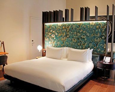Descubra la elegancia de una habitación moderna en el Hotel Mercer (Sevilla), que incluye una cama grande con un cabecero ornamentado, un pequeño escritorio con espejo y una iluminación cálida para una relajación y comodidad máximas. - ForTwo - Planes para parejas