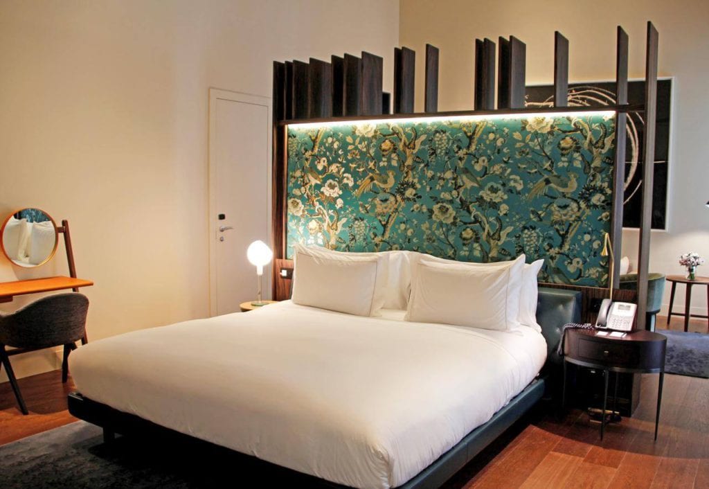 Descubra la elegancia de una habitación moderna en el Hotel Mercer (Sevilla), que incluye una cama grande con un cabecero ornamentado, un pequeño escritorio con espejo y una iluminación cálida para una relajación y comodidad máximas. - ForTwo - Planes para parejas