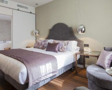 Descubra la elegancia del Hotel Palacete de Álamos Málaga: disfrute de una elegante habitación con una cama tamaño king, detalles en morado, cómodas sillas y un moderno baño abierto con una lujosa bañera para la combinación perfecta de comodidad y sofisticación. - ForTwo - Planes para parejas
