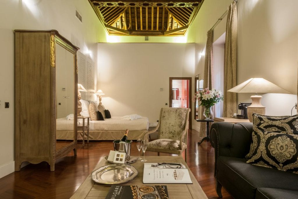 Disfrute de un retiro de lujo en el Hotel Palacio de Pinello Sevilla, donde el dormitorio cuenta con un techo de madera, muebles elegantes, una cama acogedora y una iluminación suave en el corazón de Sevilla. - ForTwo - Planes para parejas