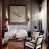 El elegante dormitorio del Hotel Palacio de Villapanés Sevilla incluye dos camas individuales, grandes obras de arte abstracto, puertas de madera ornamentadas y sillas, realzadas por una iluminación suave y flores que le añaden encanto. - ForTwo - Planes para parejas