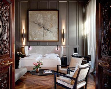 El elegante dormitorio del Hotel Palacio de Villapanés Sevilla incluye dos camas individuales, grandes obras de arte abstracto, puertas de madera ornamentadas y sillas, realzadas por una iluminación suave y flores que le añaden encanto. - ForTwo - Planes para parejas