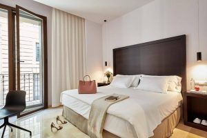 Disfrute de una moderna habitación en el Hotel Posada del Lucero Sevilla, con una amplia cama con mesitas de noche, una silla y un acogedor bolso sobre la cama. Las puertas del balcón le permiten disfrutar del animado ambiente sevillano desde su habitación. - ForTwo - Planes para parejas