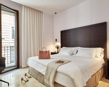 Disfrute de una moderna habitación en el Hotel Posada del Lucero Sevilla, con una amplia cama con mesitas de noche, una silla y un acogedor bolso sobre la cama. Las puertas del balcón le permiten disfrutar del animado ambiente sevillano desde su habitación. - ForTwo - Planes para parejas
