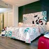 Una moderna habitación de hotel con una cama con estampado floral, una pared con acento oscuro, un piso de madera y una maleta roja prepara el escenario para una 'Escapada 50 Sombras de gris con Spa, lovebox, Jacuzzi privado (Murcia)', que ofrece una estadía intrigante y lujosa. - ForTwo - Planes para parejas