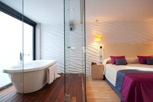 Una habitación del Hotel Vincci Selección Posada del Patio Málaga ofrece una bañera independiente, paredes texturizadas, una cama acogedora y almohadas vibrantes, combinando a la perfección estilo y comodidad. - ForTwo - Planes para parejas