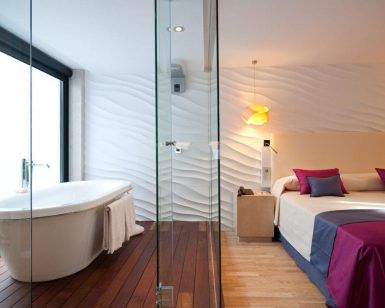 Una habitación del Hotel Vincci Selección Posada del Patio Málaga ofrece una bañera independiente, paredes texturizadas, una cama acogedora y almohadas vibrantes, combinando a la perfección estilo y comodidad. - ForTwo - Planes para parejas