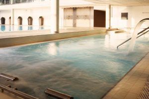 Una piscina cubierta con cascadas de agua y plantas en macetas ofrece un refugio sereno que recuerda la tranquilidad que se encuentra en el spa Día romántico del Hyatt Regency Barcelona, perfecto para relajarse antes de disfrutar de un delicioso almuerzo. - ForTwo - Planes para parejas