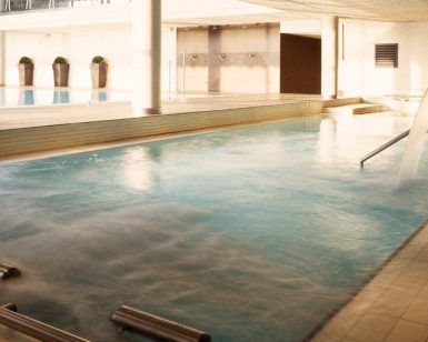 Una piscina cubierta con cascadas de agua y plantas en macetas ofrece un refugio sereno que recuerda la tranquilidad que se encuentra en el spa Día romántico del Hyatt Regency Barcelona, perfecto para relajarse antes de disfrutar de un delicioso almuerzo. - ForTwo - Planes para parejas