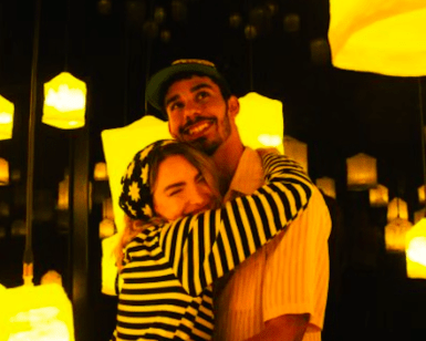 Una pareja se abraza y sonríe en medio del encantador resplandor de los faroles amarillos en la sala tenuemente iluminada de IKONO Madrid con sus Entradas para IKONO Madrid. - ForTwo - Planes para parejas
