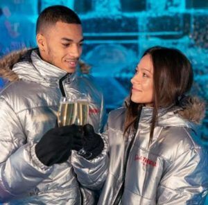 Dentro de ICEBARCELONA, una pareja con chaquetas plateadas choca sus copas, sus sonrisas iluminan el fondo helado de la experiencia Pack Romántico en ICEBARCELONA. - ForTwo - Planes para parejas