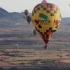 Globos aerostáticos con estampados de colores sobrevuelan el extenso paisaje de Mallorca con vistas lejanas a las montañas. Participa en un vuelo en globo compartido (Mallorca) para vivir una aventura inolvidable en este impresionante paisaje. - ForTwo - Planes para parejas