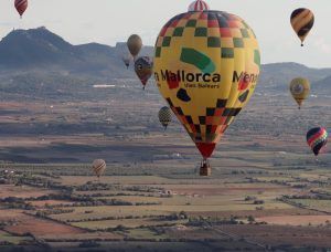 Globos aerostáticos con estampados de colores sobrevuelan el extenso paisaje de Mallorca con vistas lejanas a las montañas. Participa en un vuelo en globo compartido (Mallorca) para vivir una aventura inolvidable en este impresionante paisaje. - ForTwo - Planes para parejas