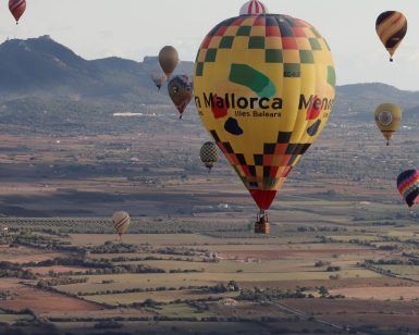 Globos aerostáticos con estampados de colores sobrevuelan el extenso paisaje de Mallorca con vistas lejanas a las montañas. Participa en un vuelo en globo compartido (Mallorca) para vivir una aventura inolvidable en este impresionante paisaje. - ForTwo - Planes para parejas