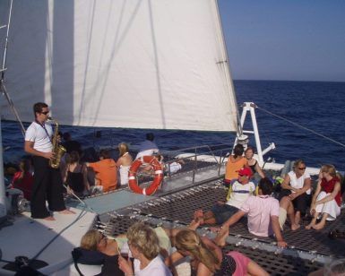 Gente relajándose con Música Jazz y chill out en un Catamarán Barcelona en el mar, mientras alguien toca melodías de jazz con un saxofón. - ForTwo - Planes para parejas