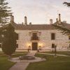 En medio del verde paisaje de Burgos, La Posada de Pradorey (Burgos) es un gran edificio histórico de piedra rodeado de árboles, que cuenta con un impresionante jardín paisajístico y acogedores bancos en el frente. - ForTwo - Planes para parejas