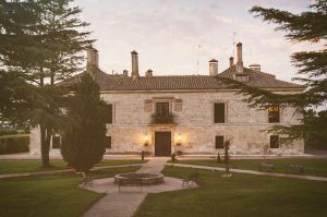 En medio del verde paisaje de Burgos, La Posada de Pradorey (Burgos) es un gran edificio histórico de piedra rodeado de árboles, que cuenta con un impresionante jardín paisajístico y acogedores bancos en el frente. - ForTwo - Planes para parejas