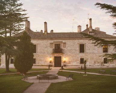 En medio del verde paisaje de Burgos, La Posada de Pradorey (Burgos) es un gran edificio histórico de piedra rodeado de árboles, que cuenta con un impresionante jardín paisajístico y acogedores bancos en el frente. - ForTwo - Planes para parejas