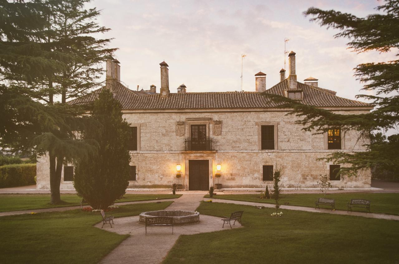En medio del verde paisaje de Burgos, La Posada de Pradorey (Burgos) es un gran edificio histórico de piedra rodeado de árboles, que cuenta con un impresionante jardín paisajístico y acogedores bancos en el frente. - ForTwo - Planes para parejas