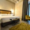 Habitación contemporánea en el Hotel Legado Alcázar de Sevilla, que cuenta con una cama grande, una silla mostaza, una mesa y una espaciosa ventana con cortinas oscuras, bellamente iluminada por lámparas de pared. - ForTwo - Planes para parejas