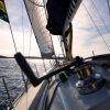 Vive la aventura perfecta de fin de semana en aguas tranquilas bajo un cielo nublado, como se ve desde la cubierta de un velero con las velas desplegadas y el timón a la vista. Quizás acabas de completar tu Curso PER de fin de semana con Cenautica (Badajoz). - ForTwo - Planes para parejas