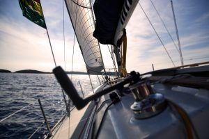 Vive la aventura perfecta de fin de semana en aguas tranquilas bajo un cielo nublado, como se ve desde la cubierta de un velero con las velas desplegadas y el timón a la vista. Quizás acabas de completar tu Curso PER de fin de semana con Cenautica (Badajoz). - ForTwo - Planes para parejas