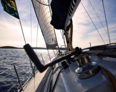 Vive la aventura perfecta de fin de semana en aguas tranquilas bajo un cielo nublado, como se ve desde la cubierta de un velero con las velas desplegadas y el timón a la vista. Quizás acabas de completar tu Curso PER de fin de semana con Cenautica (Badajoz). - ForTwo - Planes para parejas