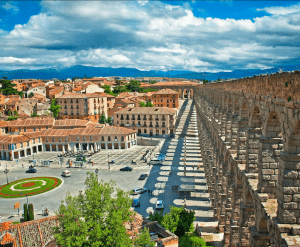 El antiguo acueducto de piedra se extiende majestuosamente por el paisaje urbano de Segovia, revelando la historia debajo del Alcázar de Segovia, presentado en "Ávila y Segovia: Excursión de un día desde Madrid con Entrada al Alcázar de Segovia", en medio de techos de terracota y un cielo parcialmente nublado. - ForTwo - Planes para parejas