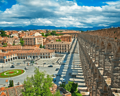 El antiguo acueducto de piedra se extiende majestuosamente por el paisaje urbano de Segovia, revelando la historia debajo del Alcázar de Segovia, presentado en "Ávila y Segovia: Excursión de un día desde Madrid con Entrada al Alcázar de Segovia", en medio de techos de terracota y un cielo parcialmente nublado. - ForTwo - Planes para parejas