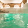 Relájese en el spa del Hotel Hospes Puerta de Alcalá, Madrid, con aguas turquesas bajo un techo abovedado de ladrillo. Una cascada ofrece sonidos relajantes y la luz de las velas enriquece la atmósfera serena. - ForTwo - Planes para parejas