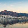 El puerto deportivo con yates y barcos atracados contra los edificios blancos y las montañas de Marbella durante la puesta de sol ofrece una vista pintoresca, como parte de un inolvidable Free tour por Marbella. - ForTwo - Planes para parejas