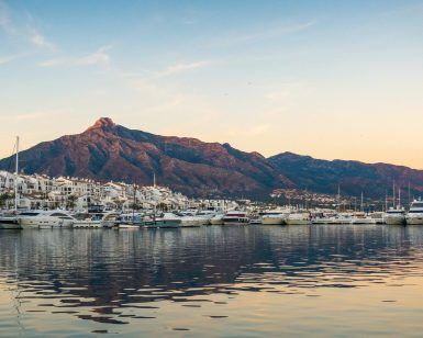 El puerto deportivo con yates y barcos atracados contra los edificios blancos y las montañas de Marbella durante la puesta de sol ofrece una vista pintoresca, como parte de un inolvidable Free tour por Marbella. - ForTwo - Planes para parejas