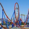 La Entrada con descuento al Parque Warner de Madrid ofrece una experiencia emocionante mientras los pasajeros recorren circuitos rojos y amarillos en una emocionante montaña rusa contra el cielo azul claro. - ForTwo - Planes para parejas