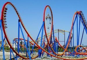 La Entrada con descuento al Parque Warner de Madrid ofrece una experiencia emocionante mientras los pasajeros recorren circuitos rojos y amarillos en una emocionante montaña rusa contra el cielo azul claro. - ForTwo - Planes para parejas