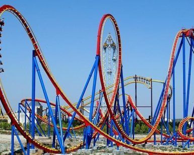 La Entrada con descuento al Parque Warner de Madrid ofrece una experiencia emocionante mientras los pasajeros recorren circuitos rojos y amarillos en una emocionante montaña rusa contra el cielo azul claro. - ForTwo - Planes para parejas