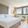 Disfrute de una moderna habitación del Hotel Meliá Princesa (Madrid) con una cama grande, una pequeña mesa redonda con dos sillas y una ventana que muestra impresionantes vistas del dinámico paisaje urbano de Madrid. - ForTwo - Planes para parejas