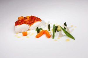 Disfrute de un plato gourmet del Menú degustación del Restaurante Montal en Zaragoza: tierno pescado con una rica salsa, bellamente adornado con zanahorias, espárragos y verduras vibrantes en un plato blanco impecable. - ForTwo - Planes para parejas