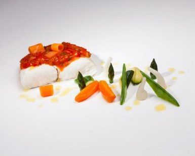 Disfrute de un plato gourmet del Menú degustación del Restaurante Montal en Zaragoza: tierno pescado con una rica salsa, bellamente adornado con zanahorias, espárragos y verduras vibrantes en un plato blanco impecable. - ForTwo - Planes para parejas