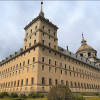 Explora un histórico edificio de piedra con ventanas arqueadas, techo abovedado y arbustos bien cuidados bajo un cielo nublado. Complementa tu visita con "Entradas al Monasterio del Escorial: Visita guiada" para apreciar plenamente su impresionante arquitectura. - ForTwo - Planes para parejas